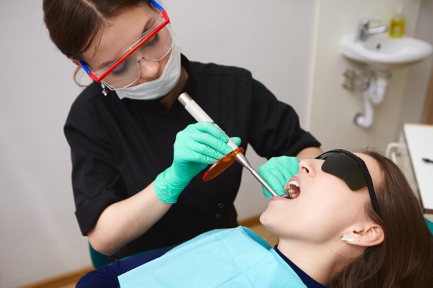 young patient black goggles getting her teeth treated by female hygienist using dental curing light 343059 402